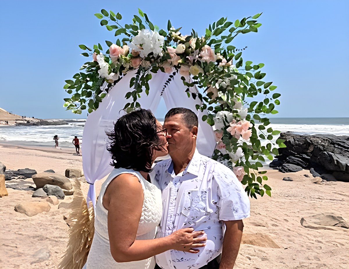 Beso bajo el arco de flores en la playa